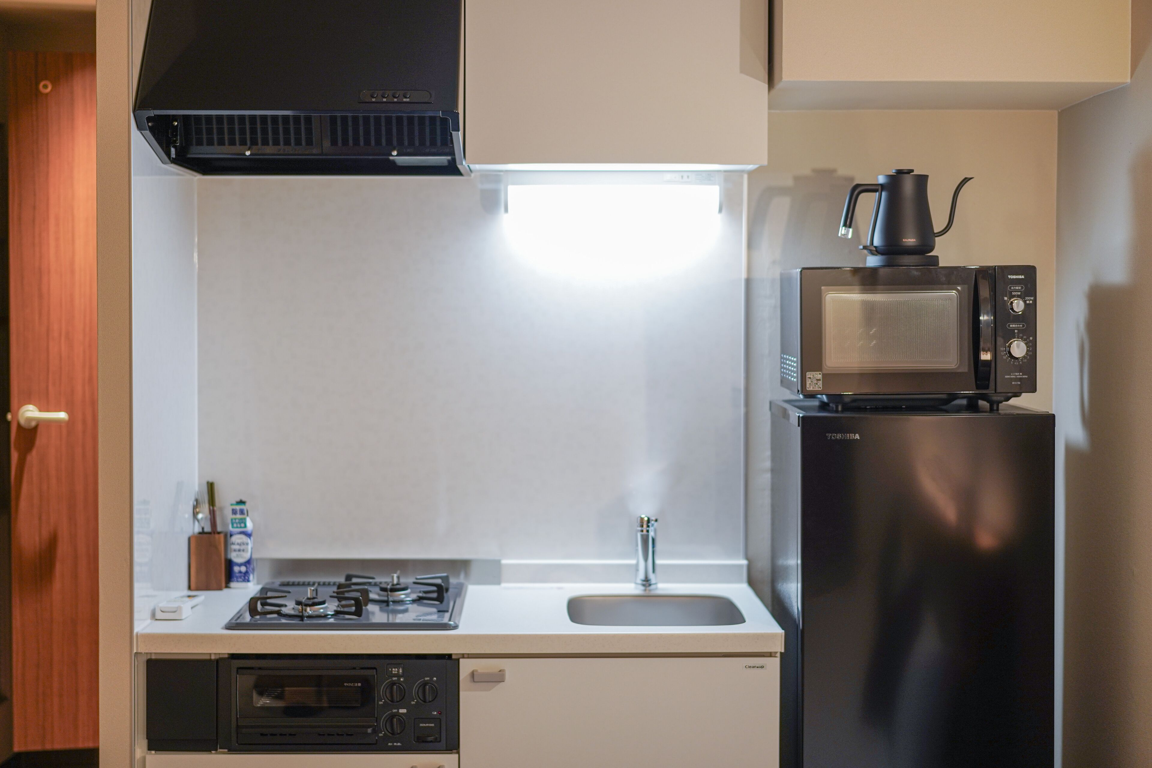 Una cucina compatta con piano cottura a gas, forno a microonde e frigorifero.