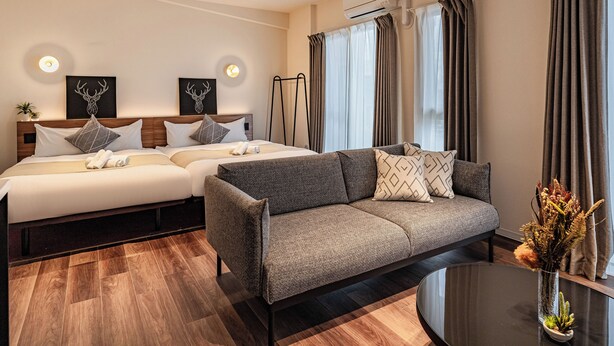Een hotelkamer met een bed, een bank, een kleintje tafeltje met een vaas en een raam met gordijnen.
