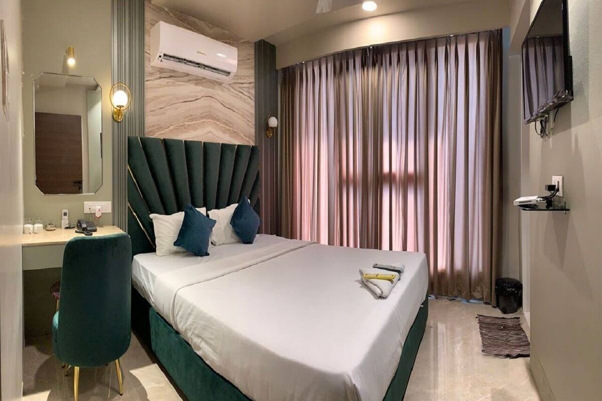 Una habitación de hotel moderna con una cama grande, un escritorio, una silla y un ventanal con cortinas.