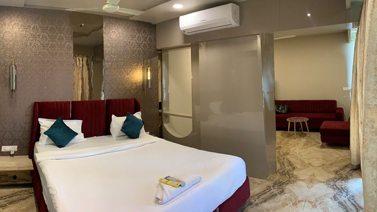 Una habitación de hotel con una cama grande, un sofá rojo, una mesita redonda y un equipo de aire acondicionado.