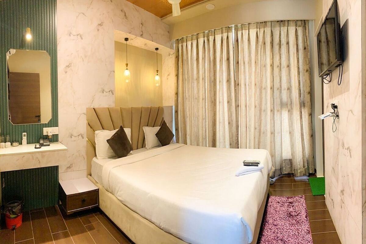 Un dormitorio con cama, mesita de noche, espejo y televisor en la pared.