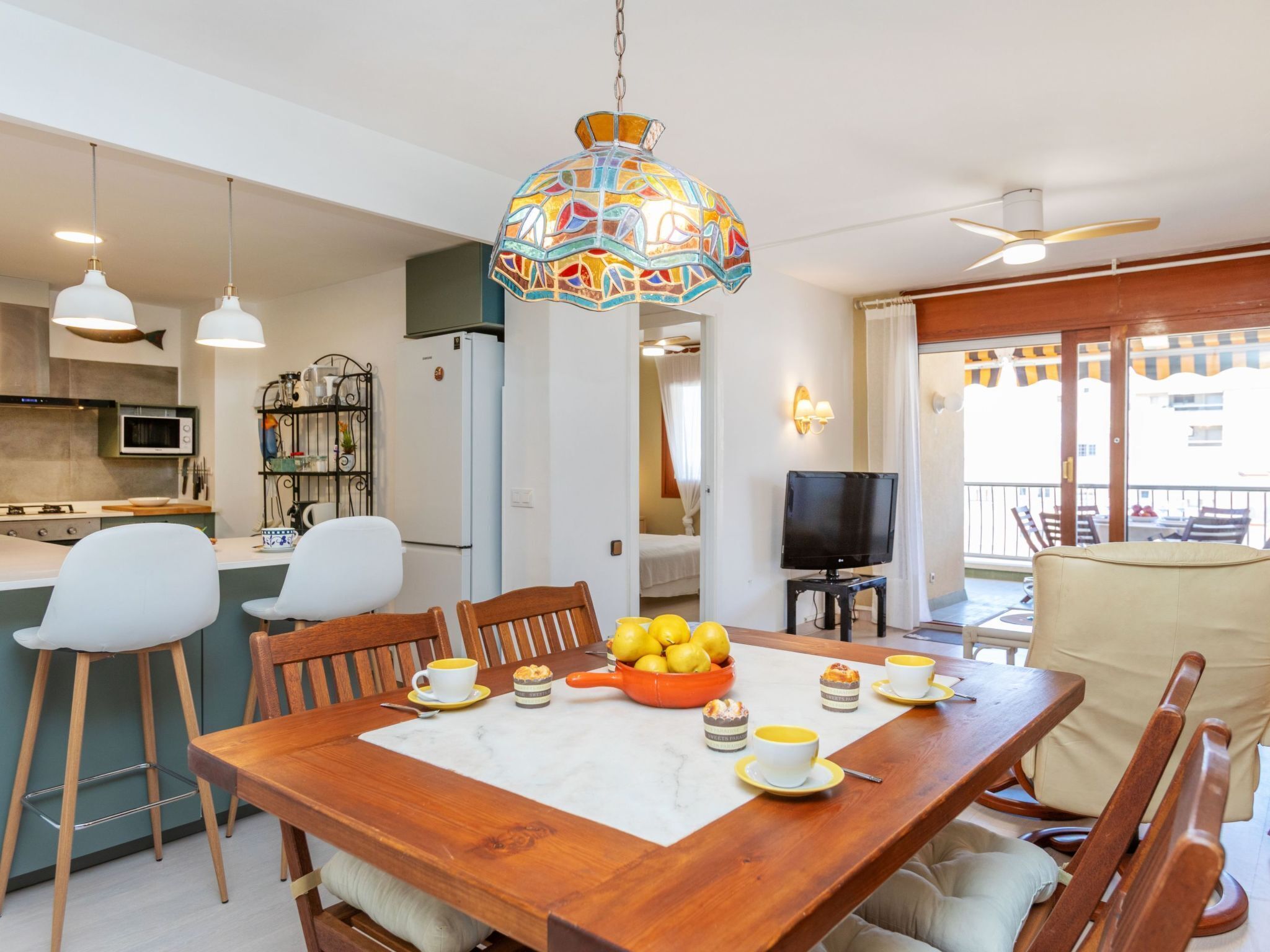A dining area with a wooden table, chairs, a chandelier, and a kitchen in the background.