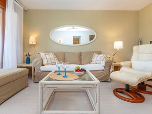 A living room with a sofa, a glass coffee table, a chair, a mirror, and a lamp.