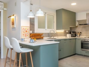 A modern kitchen with a central island, bar stools, pendant lighting, and a built-in oven.