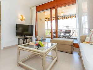 A living room with a television, a glass coffee table with fruit, a sofa, and a balcony with outdoor furniture.
