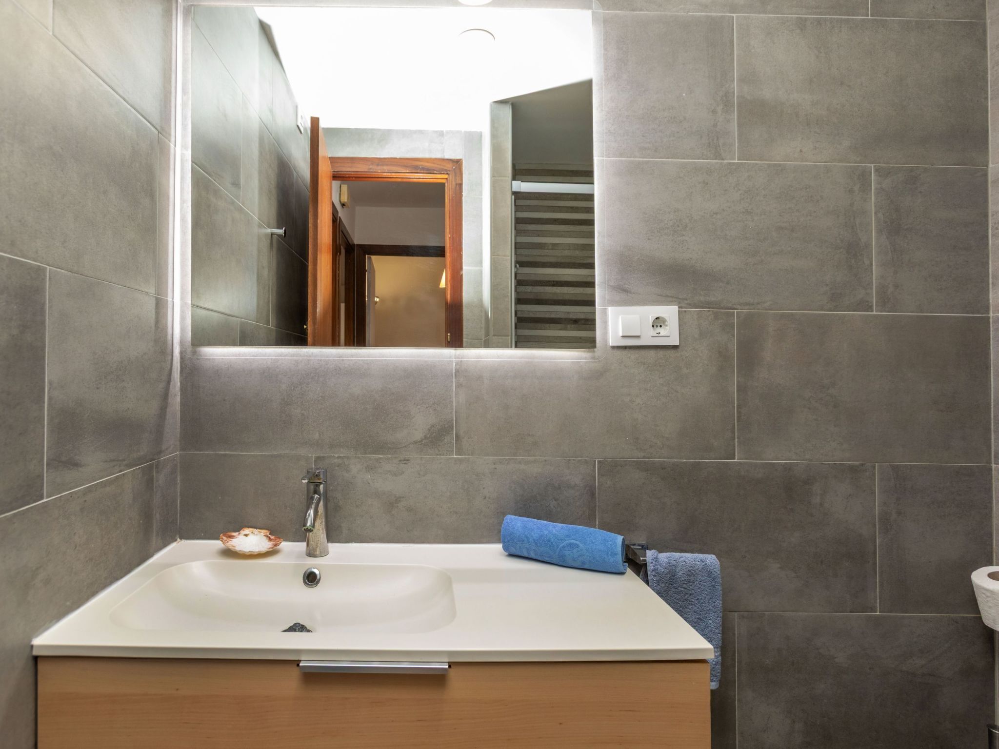 Un baño con lavamanos blanco, un espejo y un perchero para toallas.