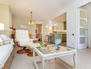 A modern living room with a glass coffee table, a white sofa, and a dining area with a bar stool.