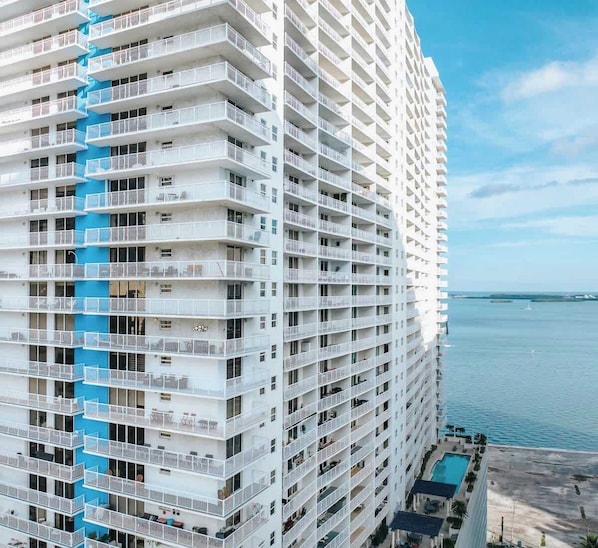 A high-rise hotel with multiple balconies, a pool area, and a view of the sea.