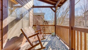 A wooden deck with rocking chairs and a patterned floor, overlooking a building and bare trees. - Bear Cove by AvantStay | Hot Tub + Pool Table | In the Heart of Pigeon Forge (Pigeon Forge)