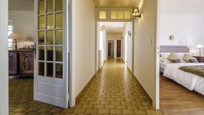 Un couloir au plancher de bois menant à une chambre à coucher équipée d’un lit et d’une table de chevet.