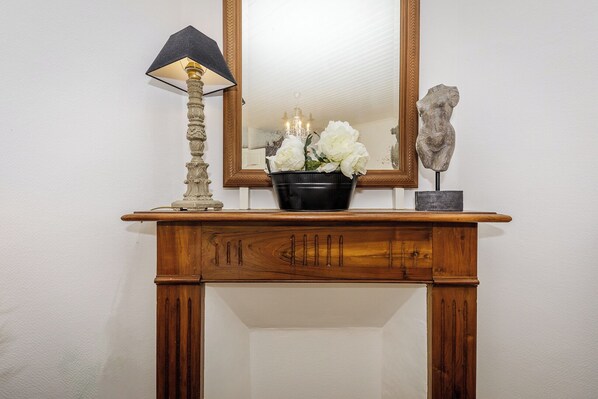 A wooden console table with a mirror above it, a lamp, and a vase with white flowers.