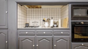 Une cuisine avec des meubles de couleur grise, un pare-feu en carreaux, une cuisinière à gaz, un four à micro-ondes et une horloge.