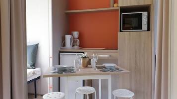 Una cocina compacta con microondas, cafetera y una pequeña estantería.