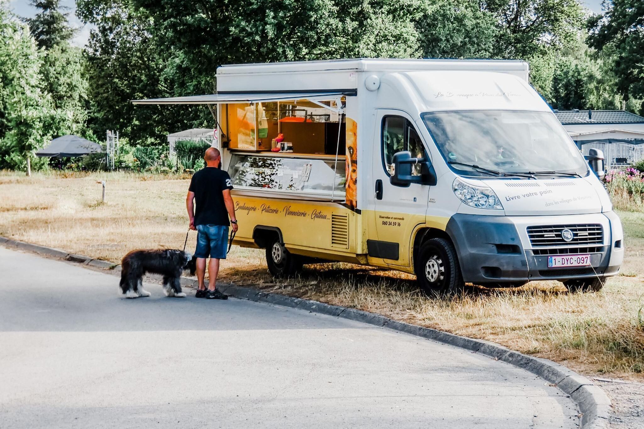 Ein Imbisswagen steht am Straßenrand, in der Nähe befinden sich eine Person und ein Hund.