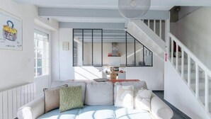 A modern living room with a white sofa, a staircase, and a kitchen in the background. - Ker Hir - Charming comfortable Breton house (Landunvez)