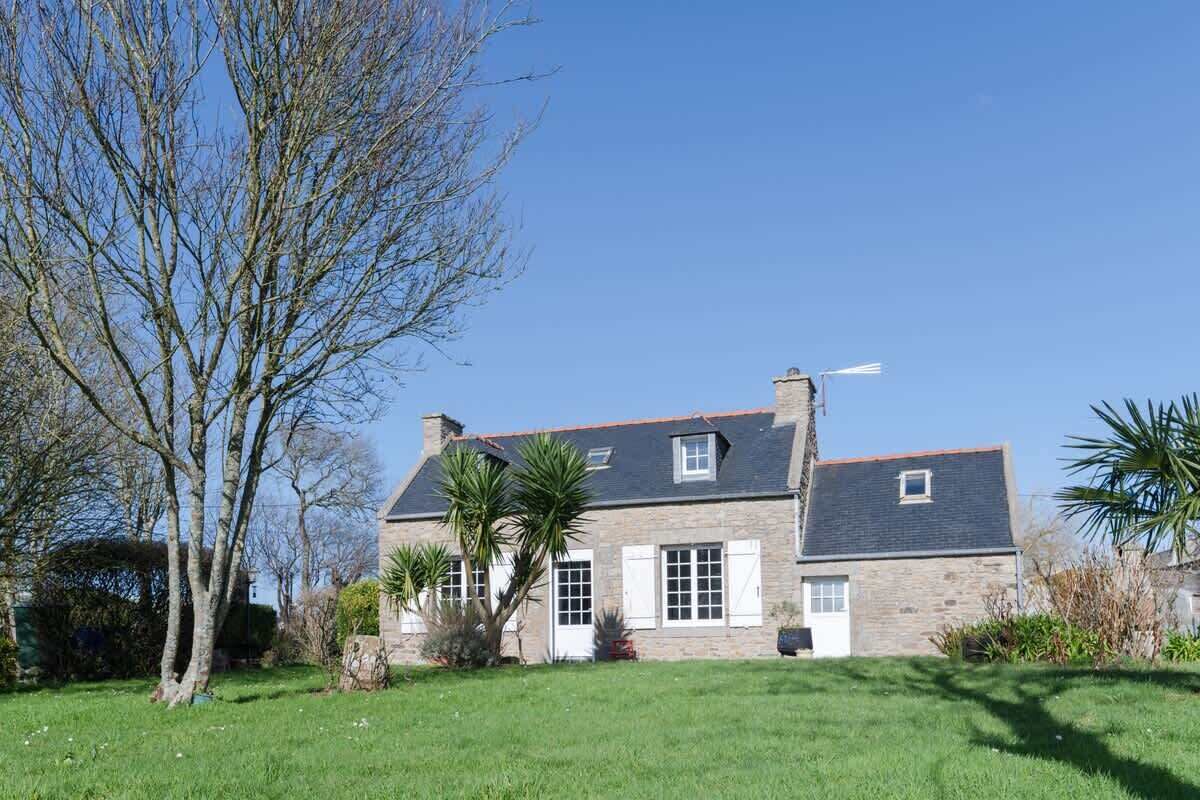 A stone house with a sloped roof, white shutters, and a chimney.