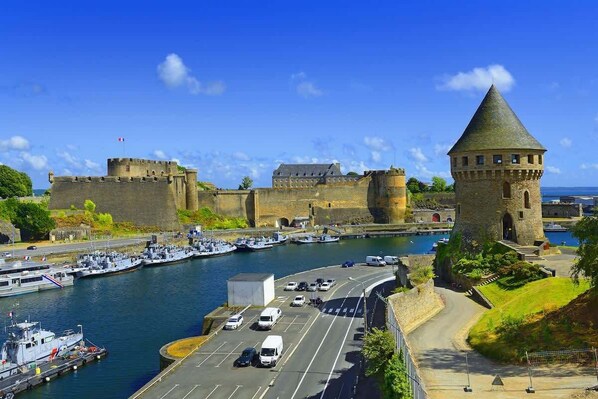 Une ville côtière dotée d’un château historique, d’un port de plaisance avec des bateaux et d’une route menant au château.