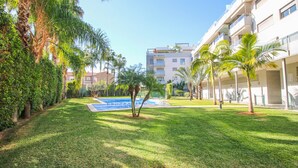 A well-maintained grassy area with a swimming pool, surrounded by palm trees and a multi-story building with balconies. - Impressive penthouse in the port of Denia. (Denia)