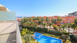A pool with a blue border, surrounded by palm trees and a building with red and white colors in the background. - Impressive penthouse in the port of Denia. (Denia)
