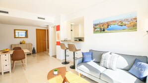 A modern living room with a grey sofa, a dining table with chairs, a kitchen area, and a large window with a cityscape view. - Impressive penthouse in the port of Denia. (Denia)