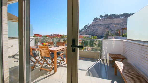 A balcony with a wooden table and chairs, a small bench, and a view of a rocky hillside. - Impressive penthouse in the port of Denia. (Denia)