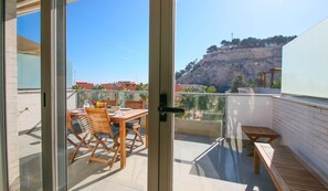 A balcony with a wooden table and chairs, a small bench, and a view of a rocky hillside. - Impressive penthouse in the port of Denia. (Denia)