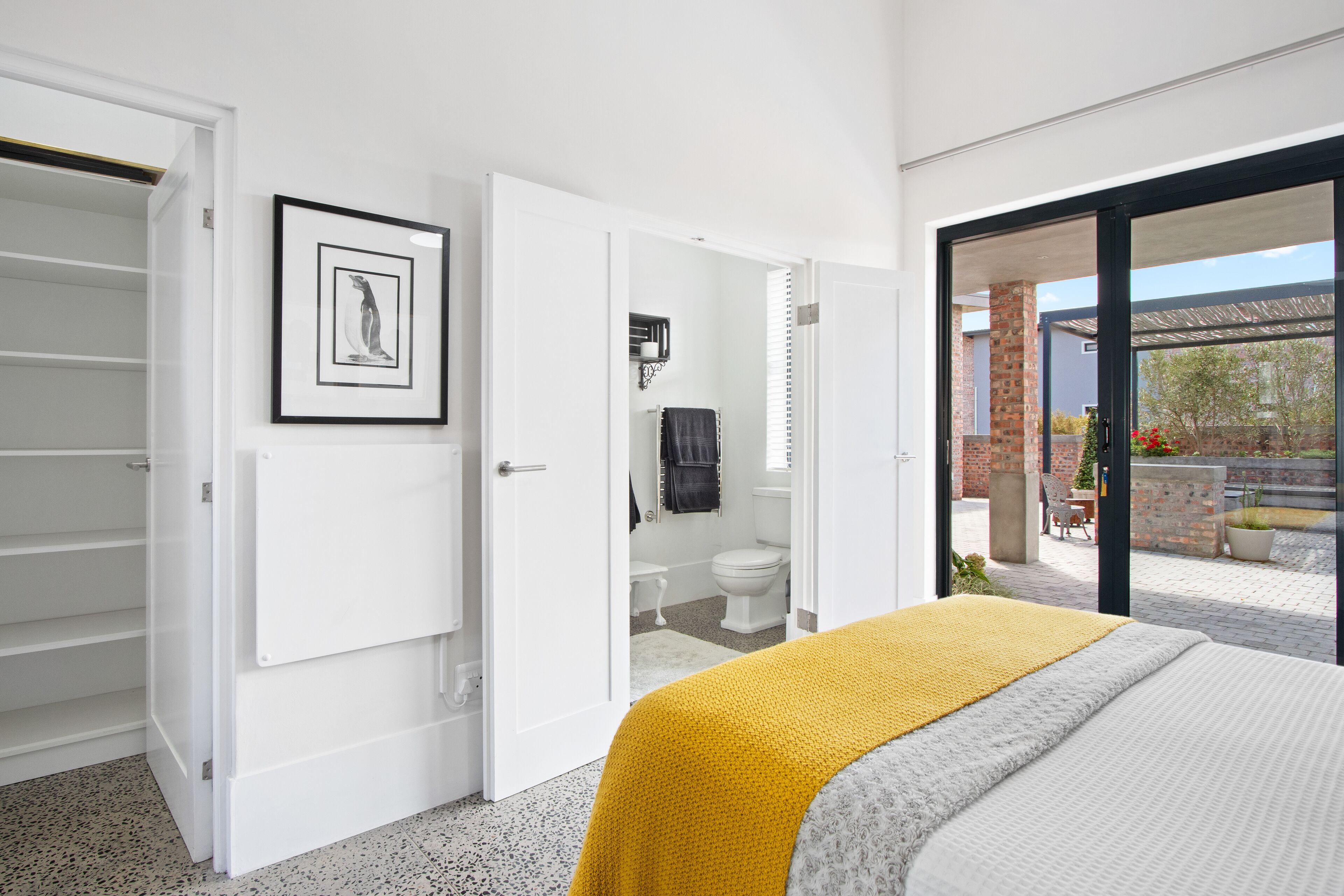 A bedroom with a bed, a white wardrobe, a bathroom with a toilet and sink, and a balcony with outdoor seating.