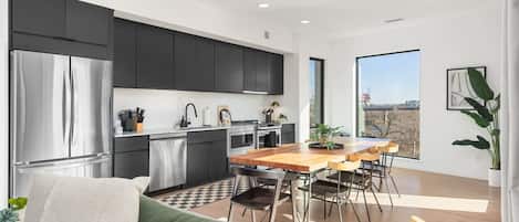 A modern kitchen with dark cabinets, stainless steel appliances, and a dining area with a wooden table and chairs.