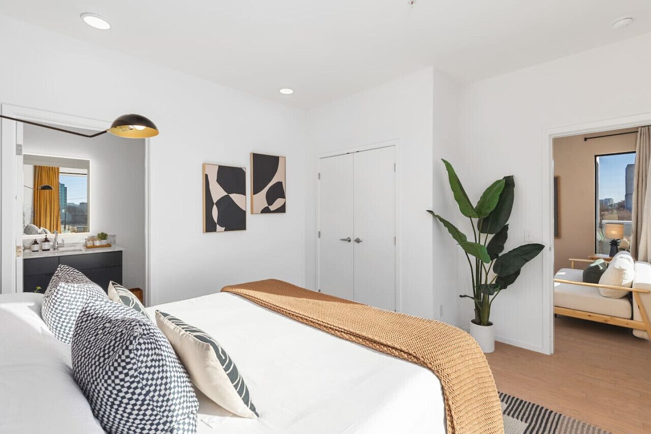 Una habitación de hotel moderna con una cama grande, una mesita de noche, un espejo y una planta en maceta.