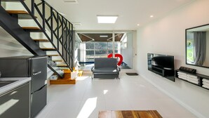 Una sala de estar moderna con cocina, una escalera, un ventanal grande y un televisor de pantalla plana.