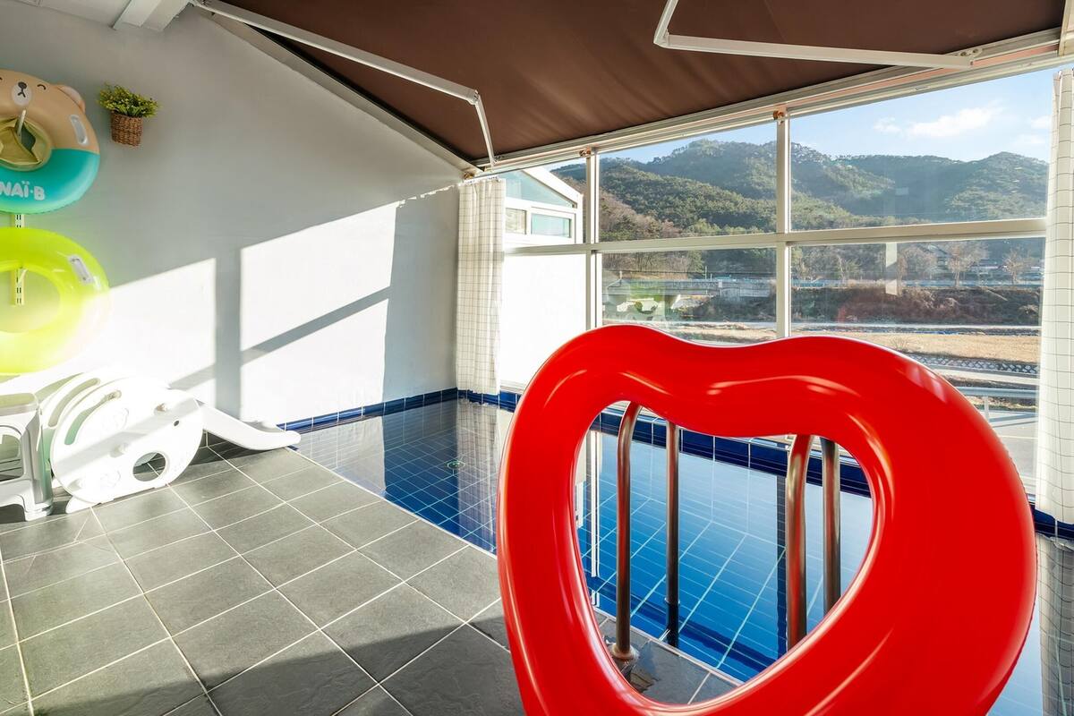 Ein Poolbereich mit einer rutsche in Herzform, einer weißen Toilette und Blick auf eine gebirgige Landschaft durch große Fenster.