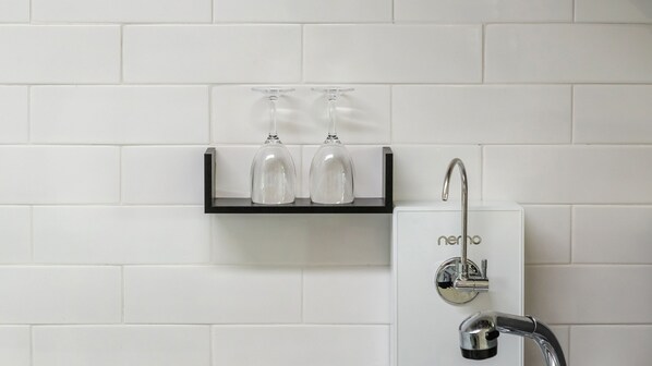A bathroom with a white tiled wall, a black shelf holding two wine glasses, and a modern faucet with the brand 'nerho'.