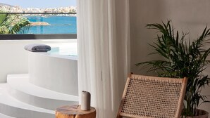 Ein Balkon mit Meerblick, eine weiße Badewanne, ein Korbstuhl und ein Topfpflanze.