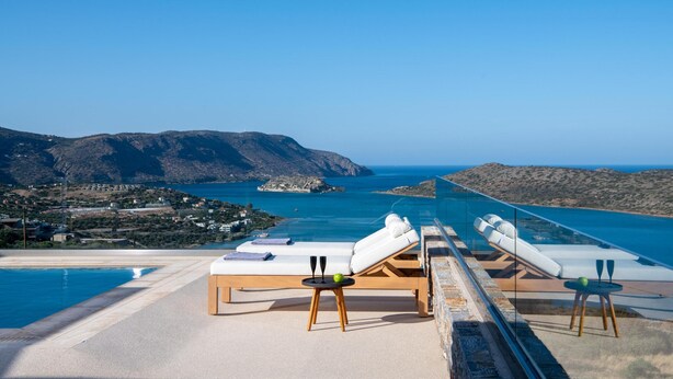 Un espace aménagé au bord de la piscine, avec des chaises longues et une balustrade en verre offrant une vue sur le paysage côtier.
