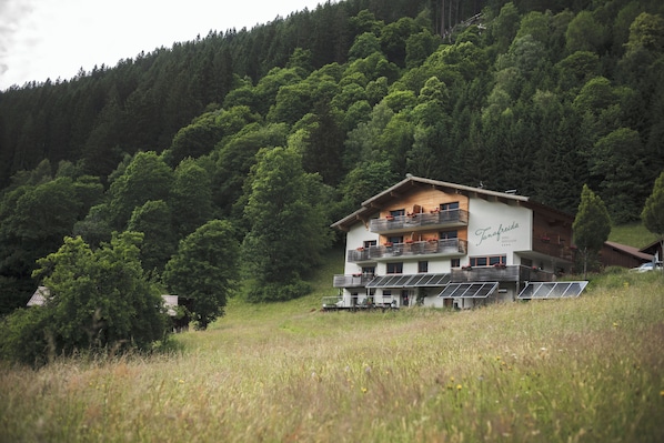 A multi-story chalet with balconies, solar panels, and a forested hillside backdrop. - Tanafreida Apartments (Sankt Gallenkirch)