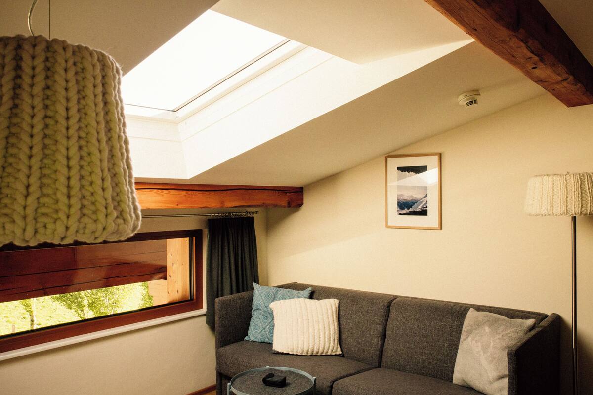 A cozy room with a sofa, a round table, a hanging light fixture, a window with curtains, and a skylight.