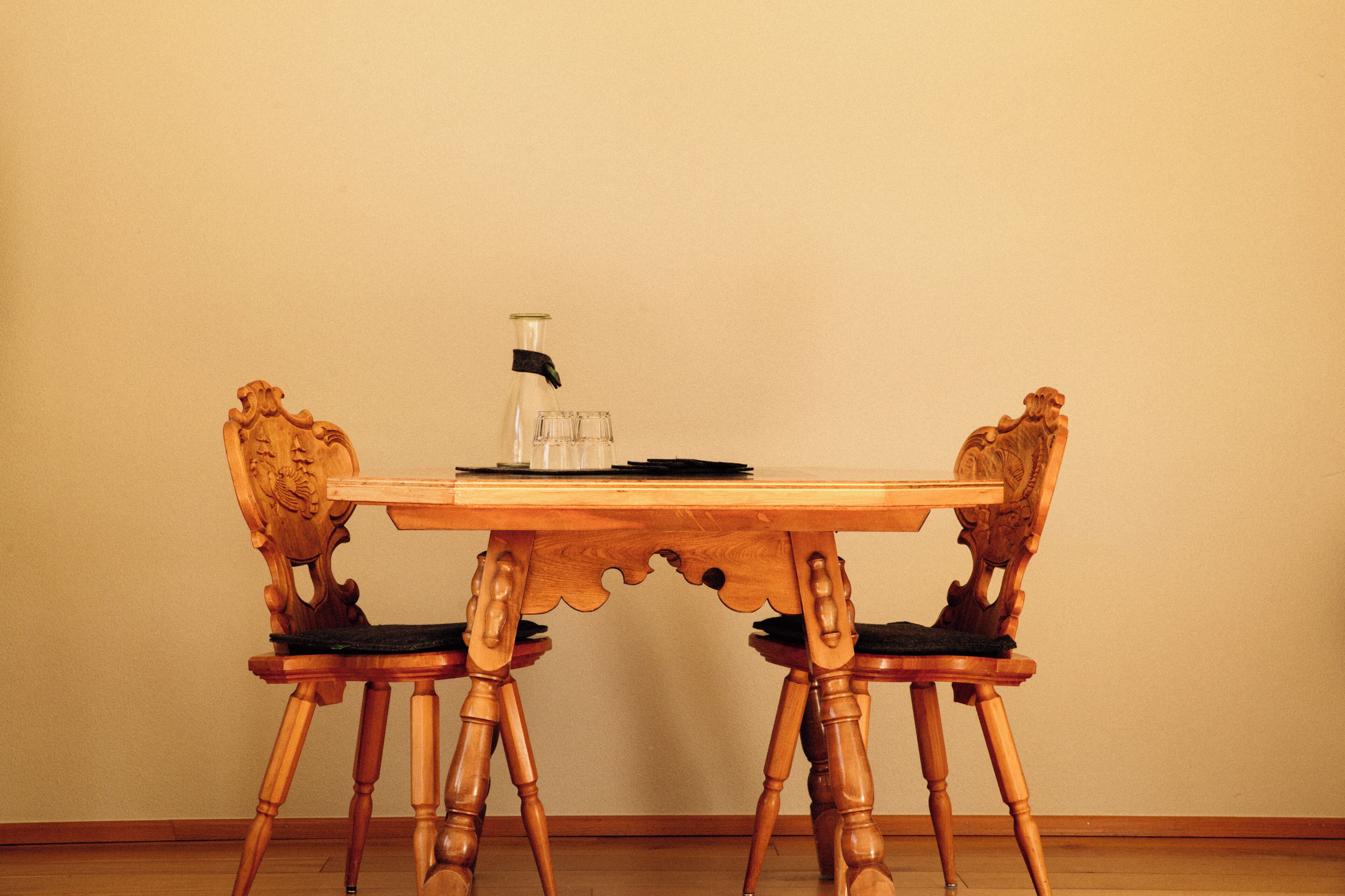 A wooden dining table with two chairs, a glass bottle, and a stack of papers.
