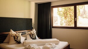 Habitación de hotel con una cama, almohadas, un ventanal con vista a follaje y una cortina.