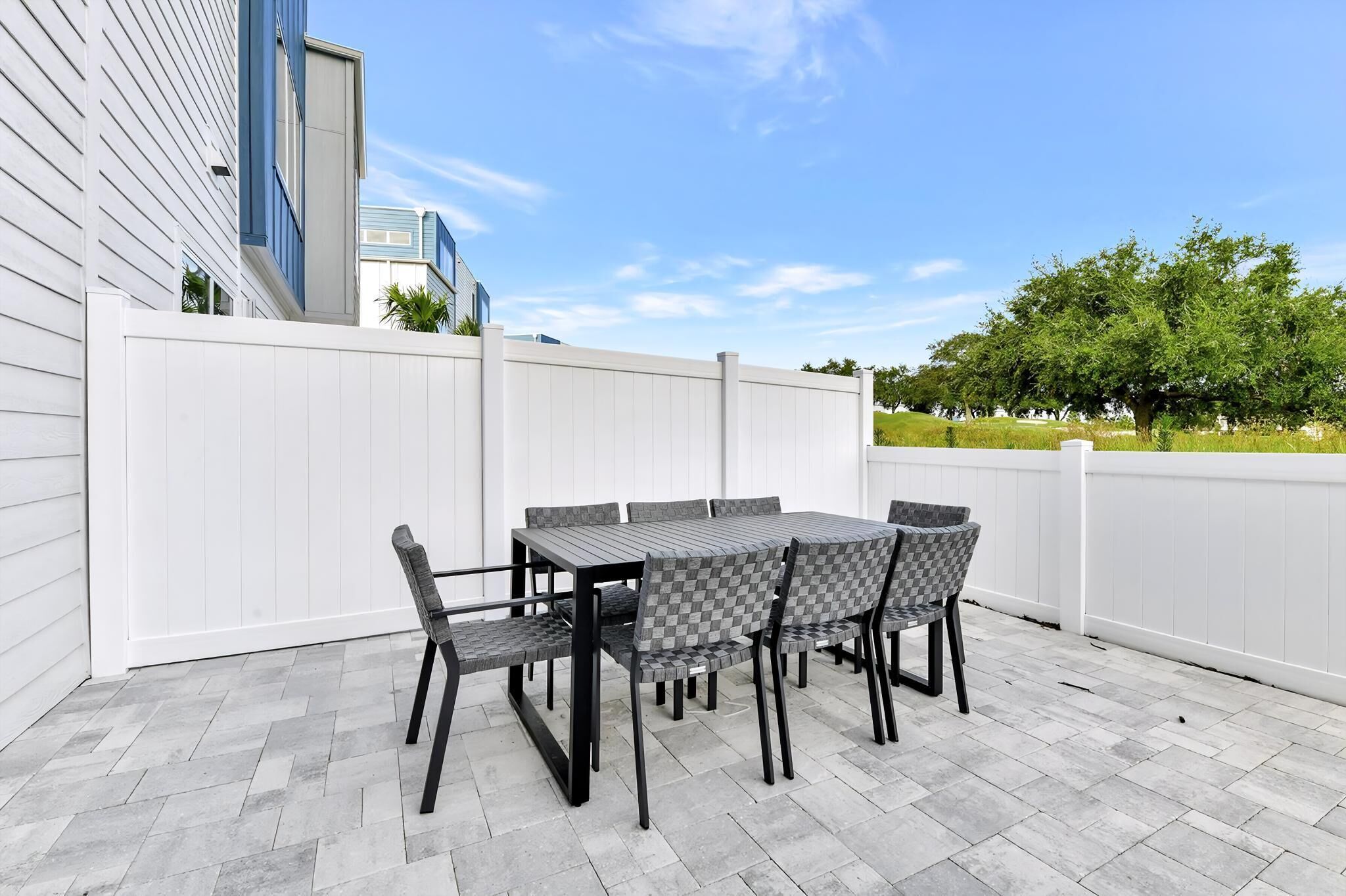 Een terras buiten met een tafel en stoelen, een wit hek en uitzicht op een gebouw en bomen.