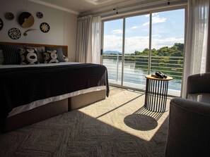 Un dormitorio con una cama grande, vistas a un lago y un balcón con mesa y silla.