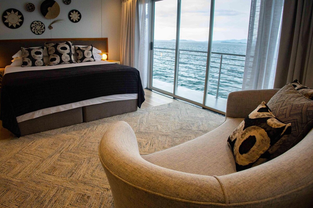 Ein Schlafzimmer mit einem Bett, einem Sofa und einem großen Fenster mit Blick auf das Meer.