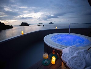 Un jacuzzi con vista al mar y a las islas, una vela y toallas sobre una mesa de madera.