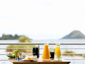 A breakfast table with a variety of food items and drinks, set against a scenic lake view.