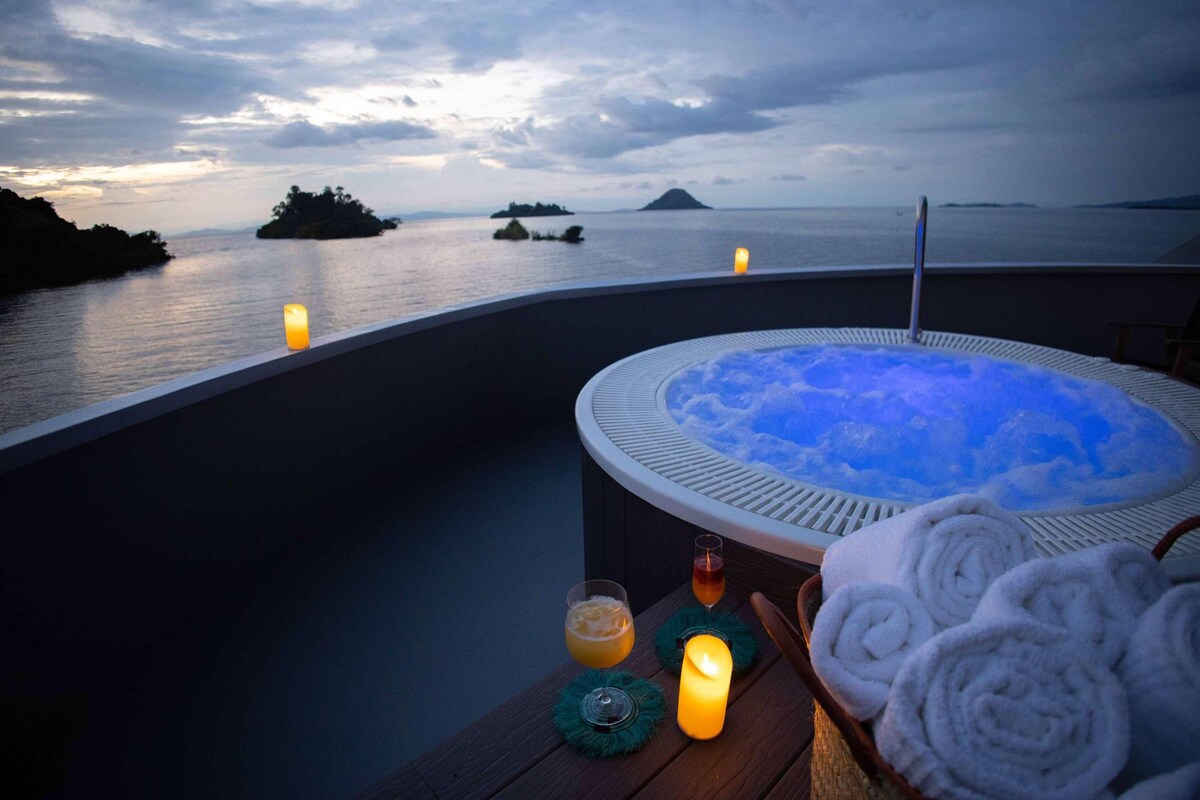 Ein Whirlpool mit Blick auf das Meer und Inseln, eine Kerze und Handtücher auf einem Holztisch.
