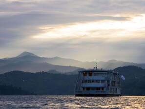 Eine Mehrdecksfähre namens Kivu Queen fährt auf ruhigem Wasser, mit einer Berglandschaft im Hintergrund.