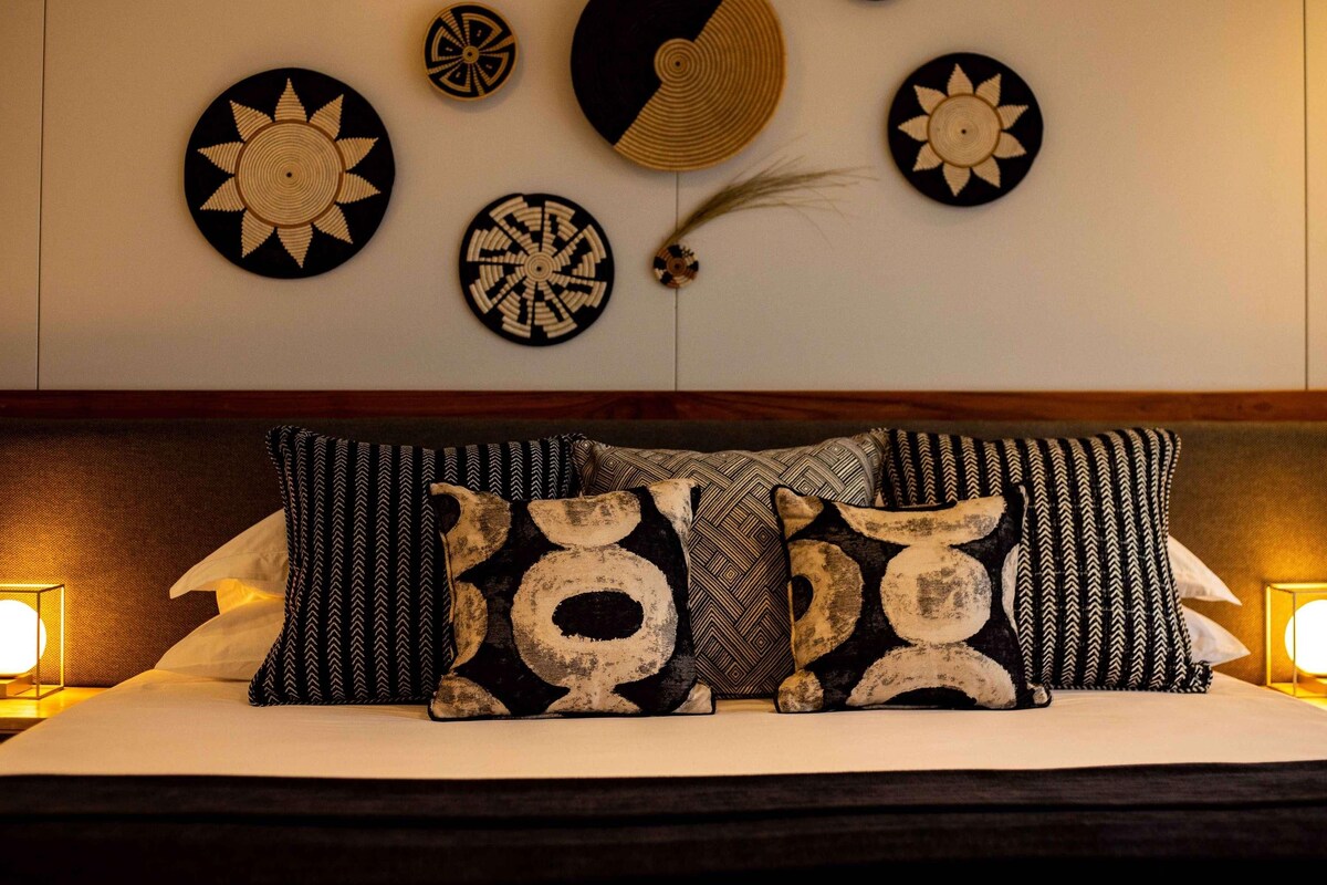 Una cama con almohadones estampados, cabecera y decoración de pared con diseños circulares y geométricos.