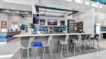 A modern bar area with a check-in counter, bar stools, and a television screen displaying a sunset.