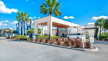A modern hotel with a covered entrance, palm trees, and a clear blue sky.