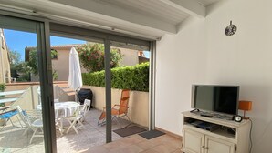 Een balkon met een televisie, een tafel, stoelen en een barbecue.