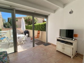 A balcony with a TV, a table, chairs, and a grill.